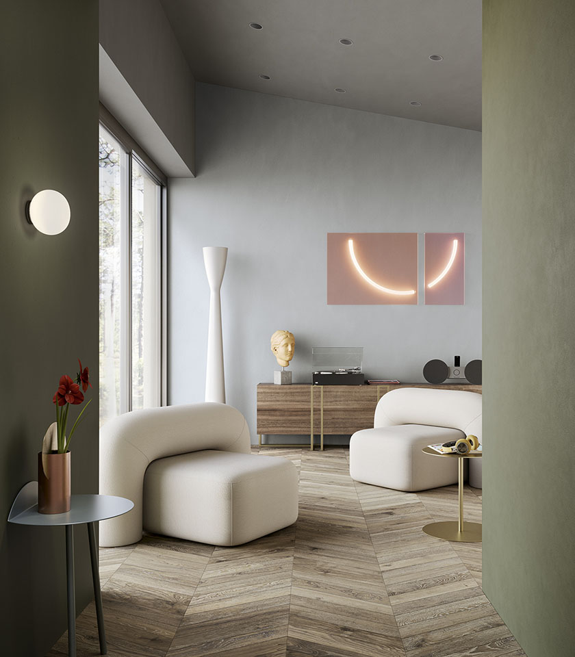 Salon contemporain avec sol effet bois en chevrons, murs vert sauge, fauteuils blancs et détails design.