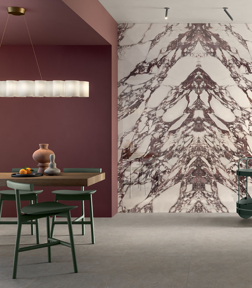 Salle à manger contemporaine avec mur décoratif effet marbre, tons bordeaux, table en bois et chaises vertes.