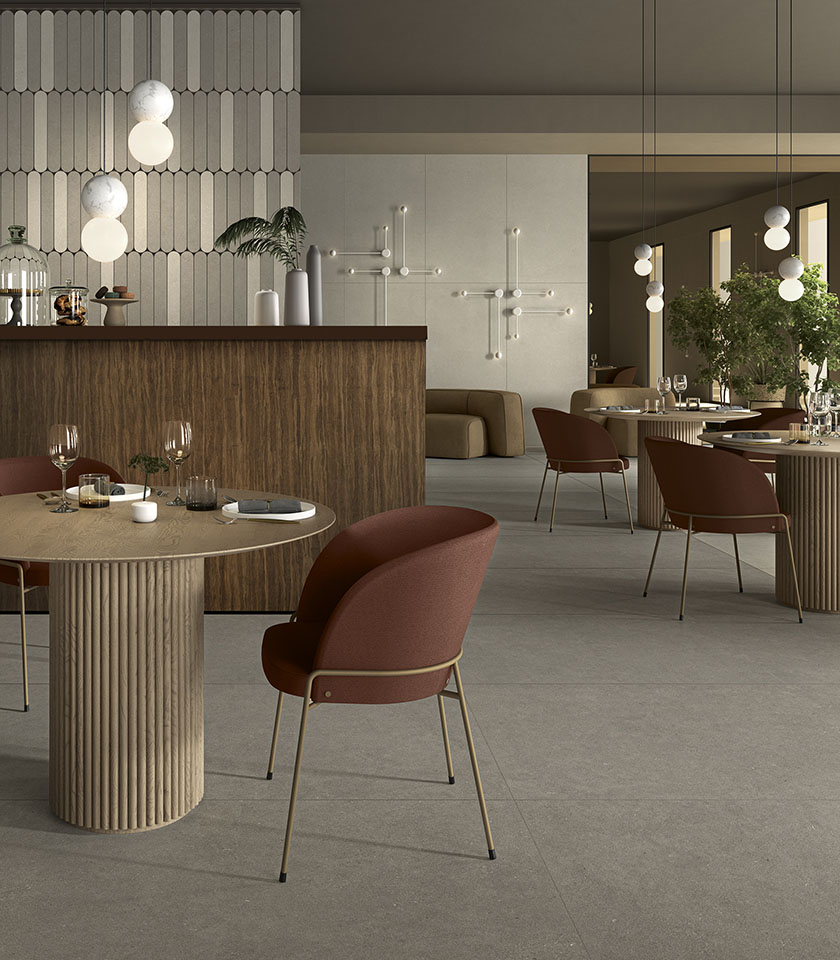 Restaurant contemporain avec sol gris effet pierre, tables sculpturales, assises bordeaux et détails en bois.