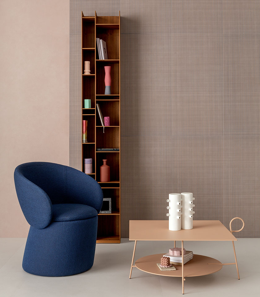 Intérieur contemporain avec fauteuil bleu, table basse aux tons poudrés, bibliothèque en bois et mur décoratif à micro-motif.