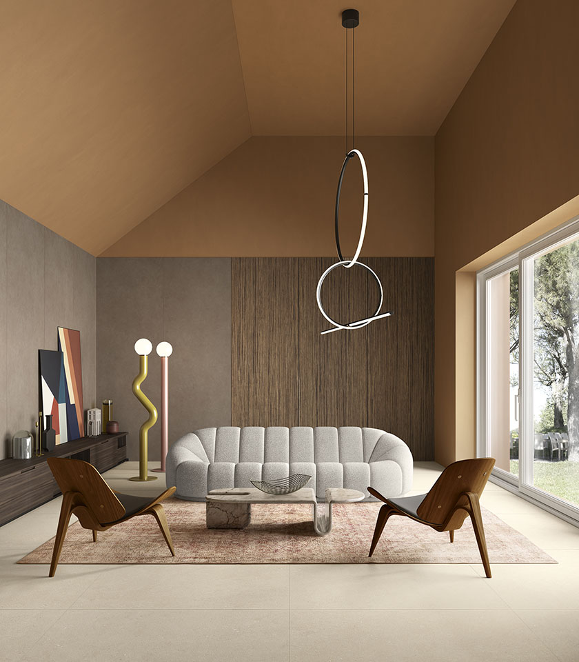 Salon contemporain avec sol beige effet pierre, canapé sculptural, fauteuils en bois et grandes baies vitrées donnant sur la verdure.