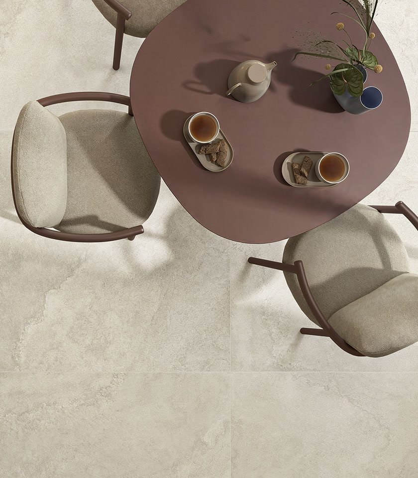 Table ronde couleur terre cuite avec service à thé et chaises rembourrées beige sur un sol de la collection Pulse, effet pierre dans la teinte Shell.