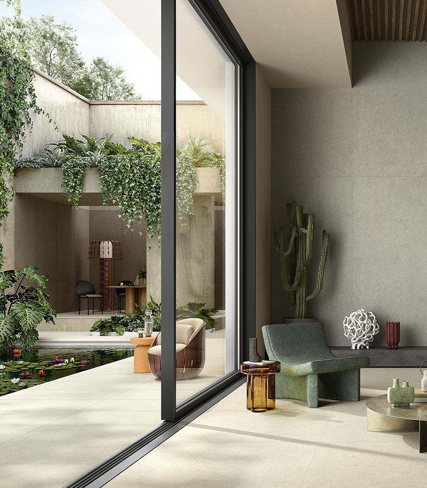 Espace intérieur-extérieur avec sol en grès cérame clair, grandes baies vitrées, végétation luxuriante et mobilier contemporain.