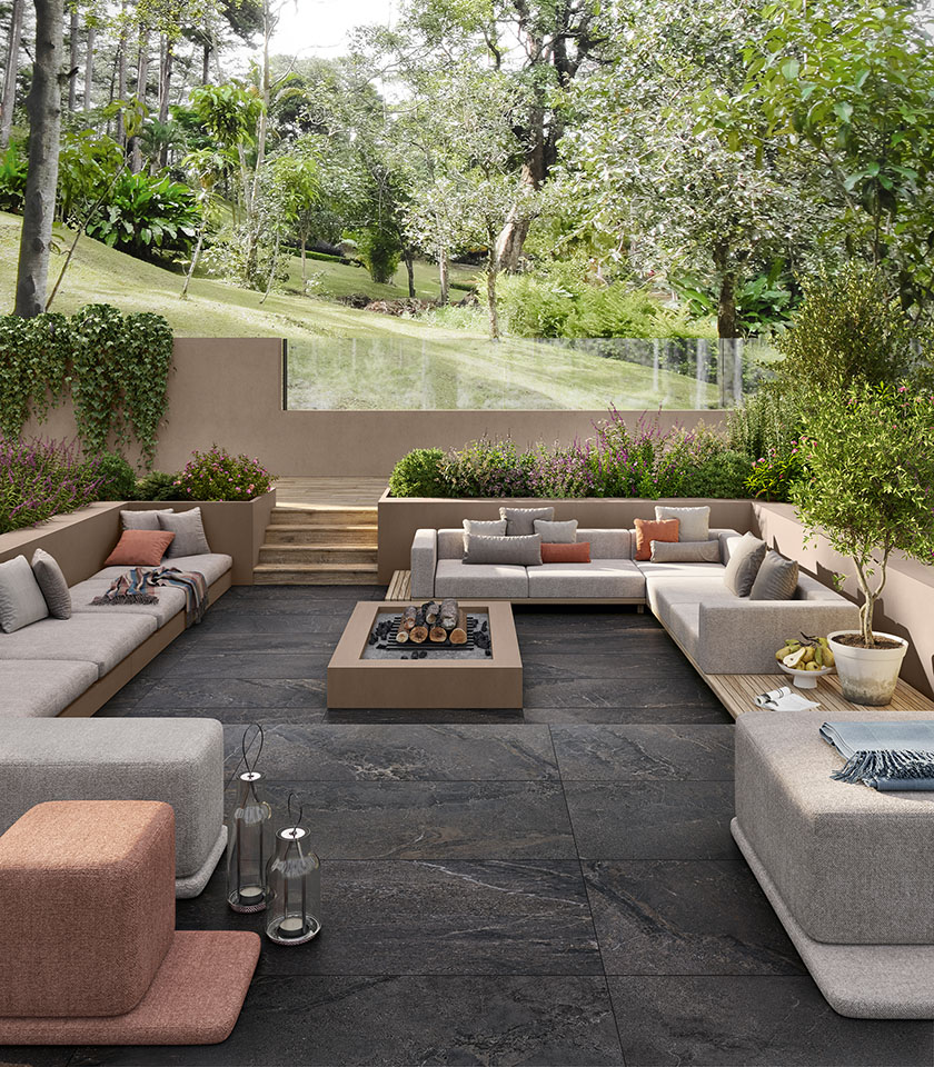 Terrasse entourée de verdure avec sol extérieur effet pierre foncée, larges assises lounge et jardinières intégrées pour un espace élégant et accueillant.