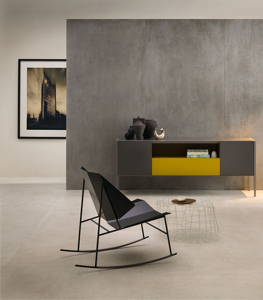 Espace de vie minimal chic avec sol clair effet béton, revêtement mural gris grand format, mobilier épuré et détails de design contemporain.