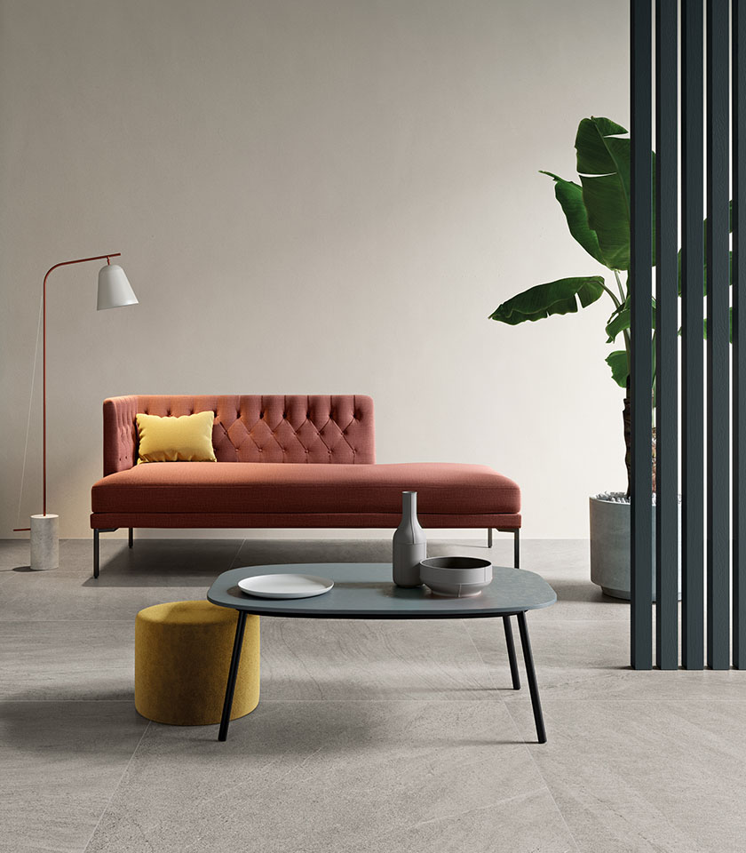 Salon minimal chic avec sol effet pierre grise, méridienne couleur terre cuite, mobilier épuré et touches chaleureuses au design contemporain.